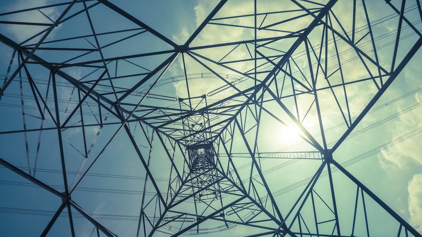 Abstract pattern from bottom view of high voltage pole power transmission tower with backlit sunshine sky background in monochrome.