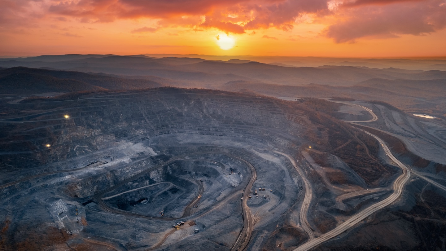 Open pit mine, extractive industry for coal. The sunsets over an cloudy orange sky in the distance.