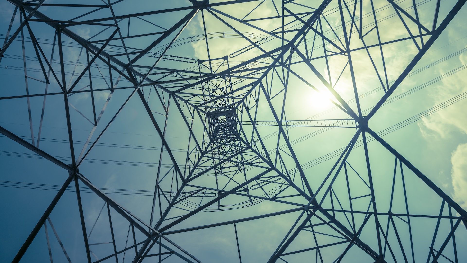 Abstract pattern from bottom view of high voltage pole power transmission tower with backlit sunshine sky background in monochrome.