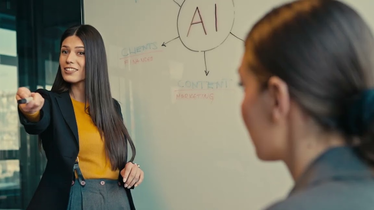 woman at whiteboard that says "AI" pointing off camera
