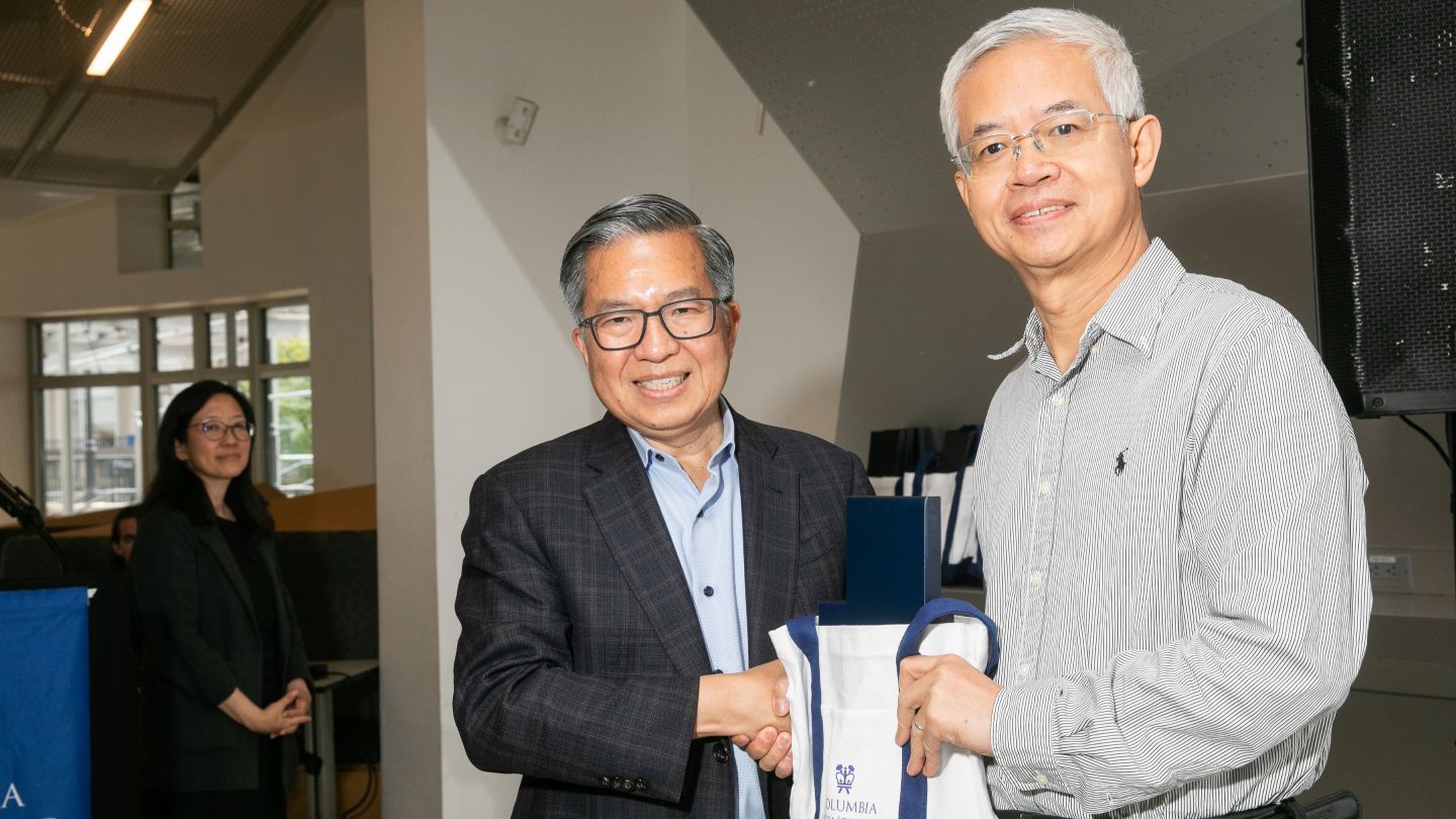 Qiang Du shakes hands with Dean Shih-Fu Chang while holding a Columbia Engineering tote bag.
