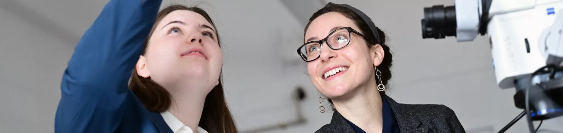 Two women. One woman holds and a microscope sample over their heads.