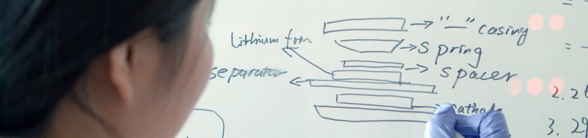 A student drawing a diagram that reads "coin cell" on a white board