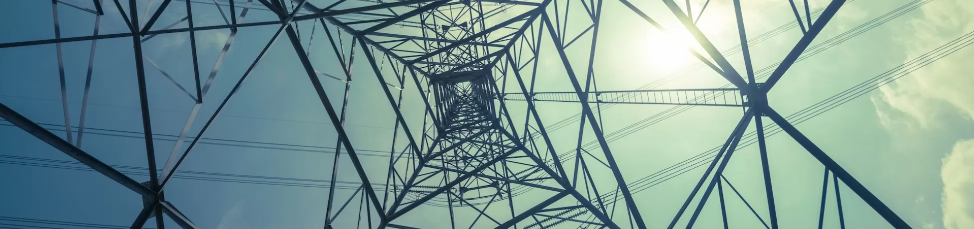 Abstract pattern from bottom view of high voltage pole power transmission tower with backlit sunshine sky background in monochrome.