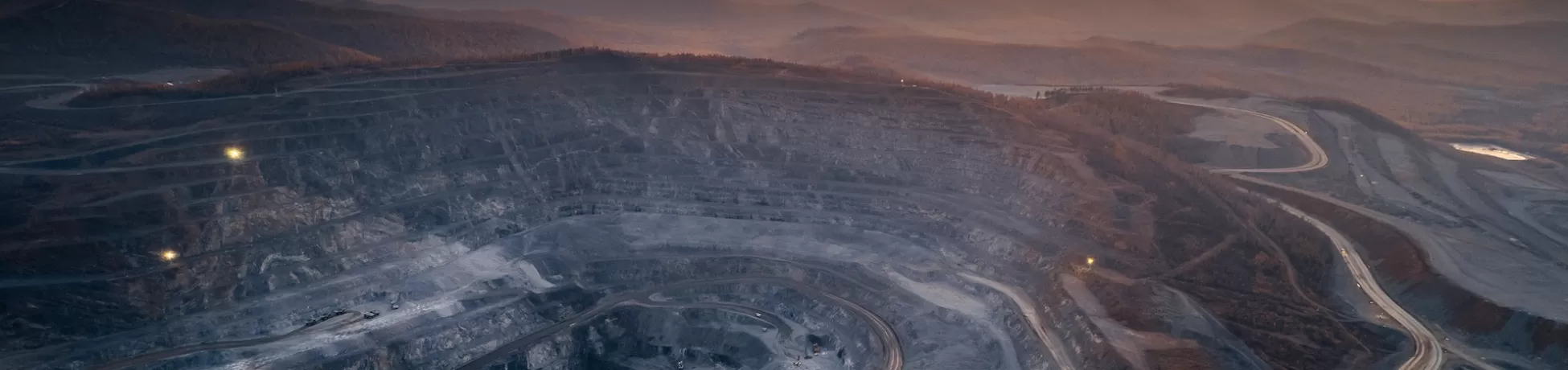 Open pit mine, extractive industry for coal. The sunsets over an cloudy orange sky in the distance.
