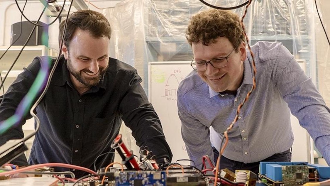Two Columbia Engineering students lean over a table to discuss a triangular robot.